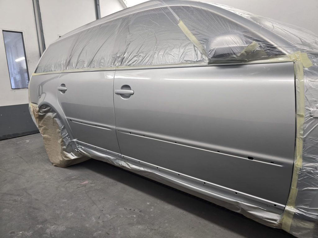 Seitliche Karosserie eines Kombis in Silber, vollständig mit Folie und Klebeband zum Lackieren der Tür vorbereitet.