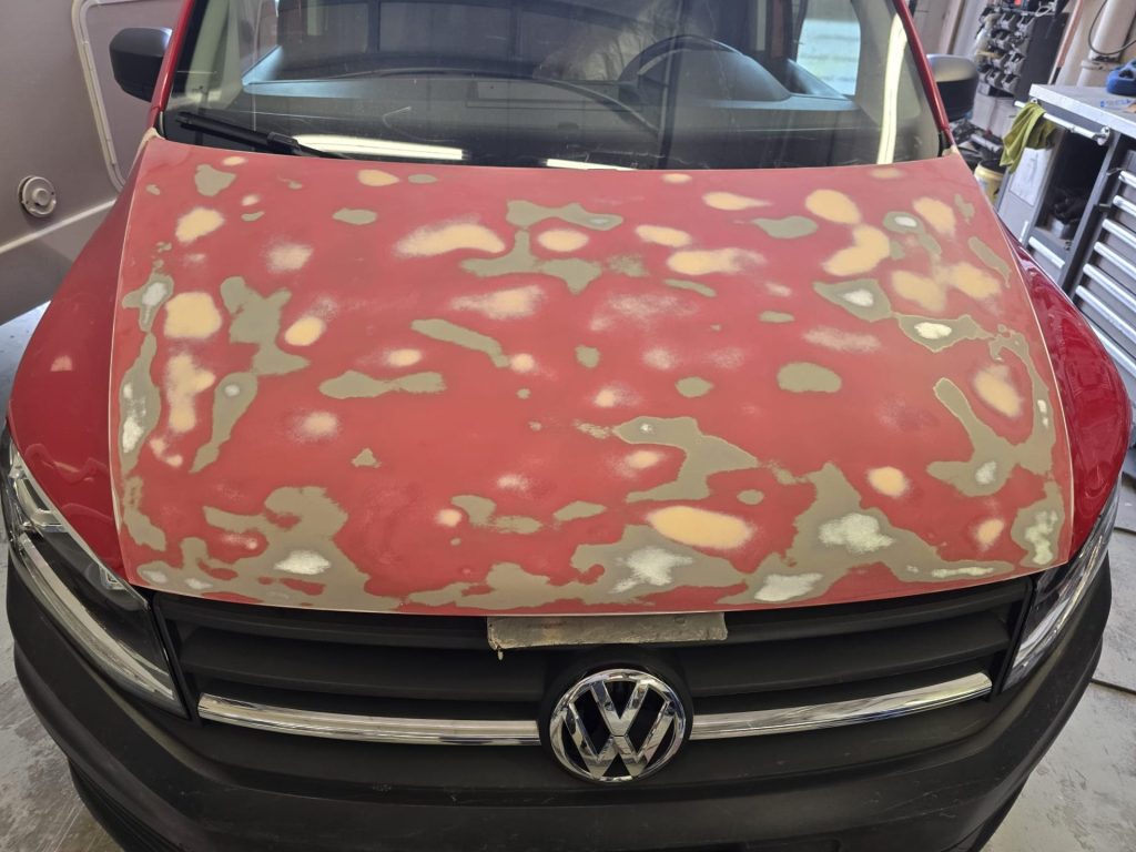 Motorhaube eines VW-Busses in Vorbereitung für die Lackierung: Spachtel- und Schleifarbeiten zur Schadensbehebung.