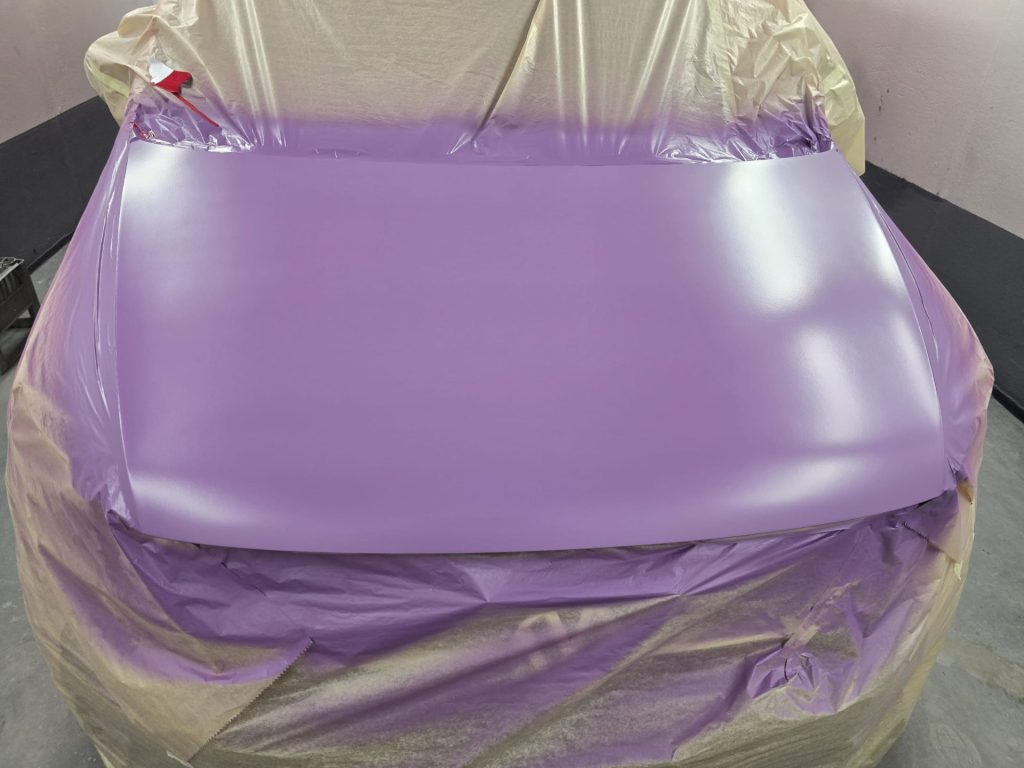 Motorhaube in der Lackierkabine, frisch grundiert mit lila Füller/Primer als Basis für den neuen Lack.