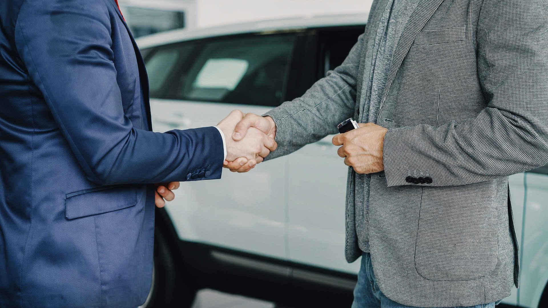 Zwei Geschäftsleute besiegeln den Deal per Handschlag in einem Autohaus.