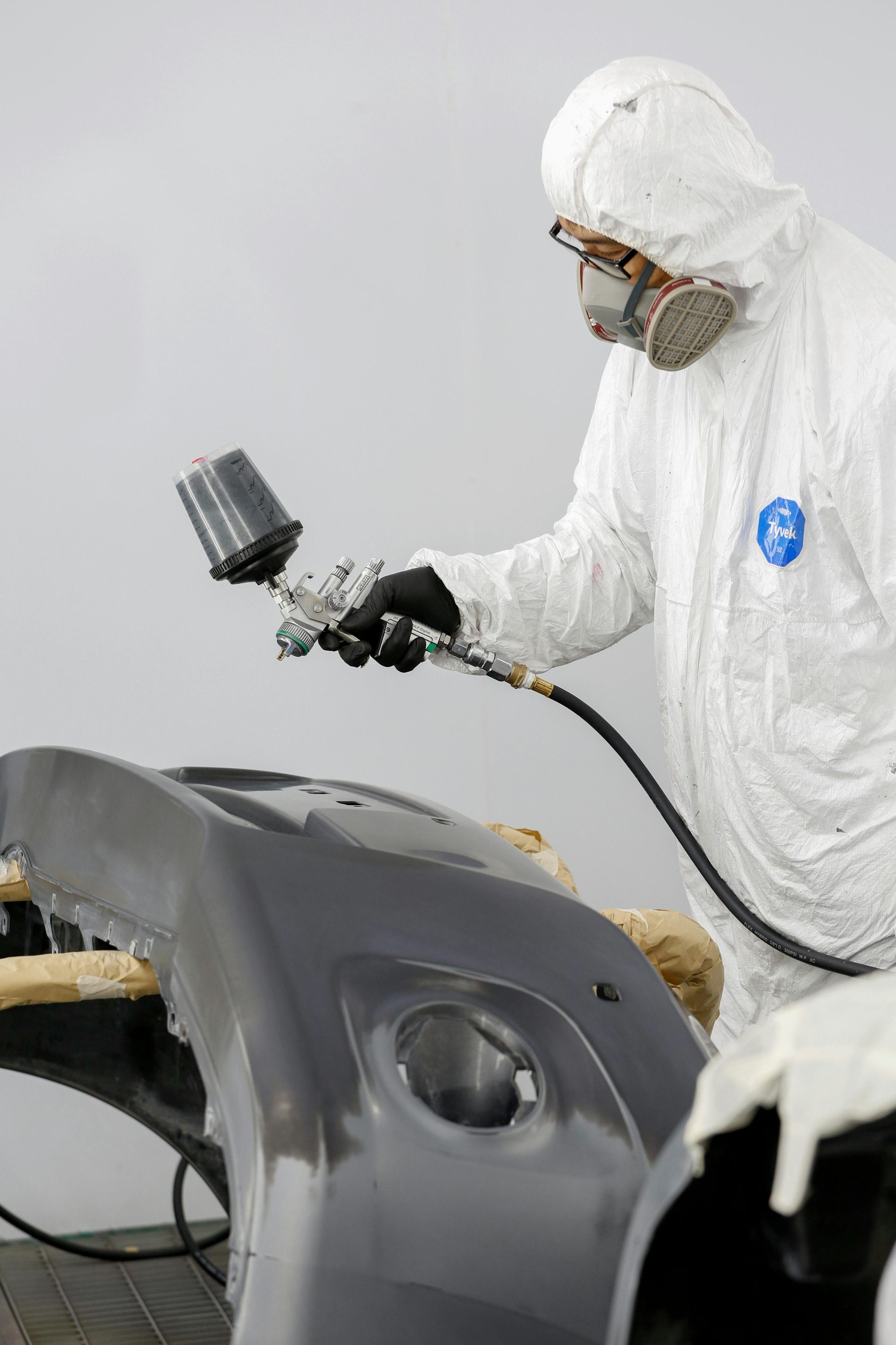 Techniker in Schutzkleidung lackiert eine Autostoßstange.